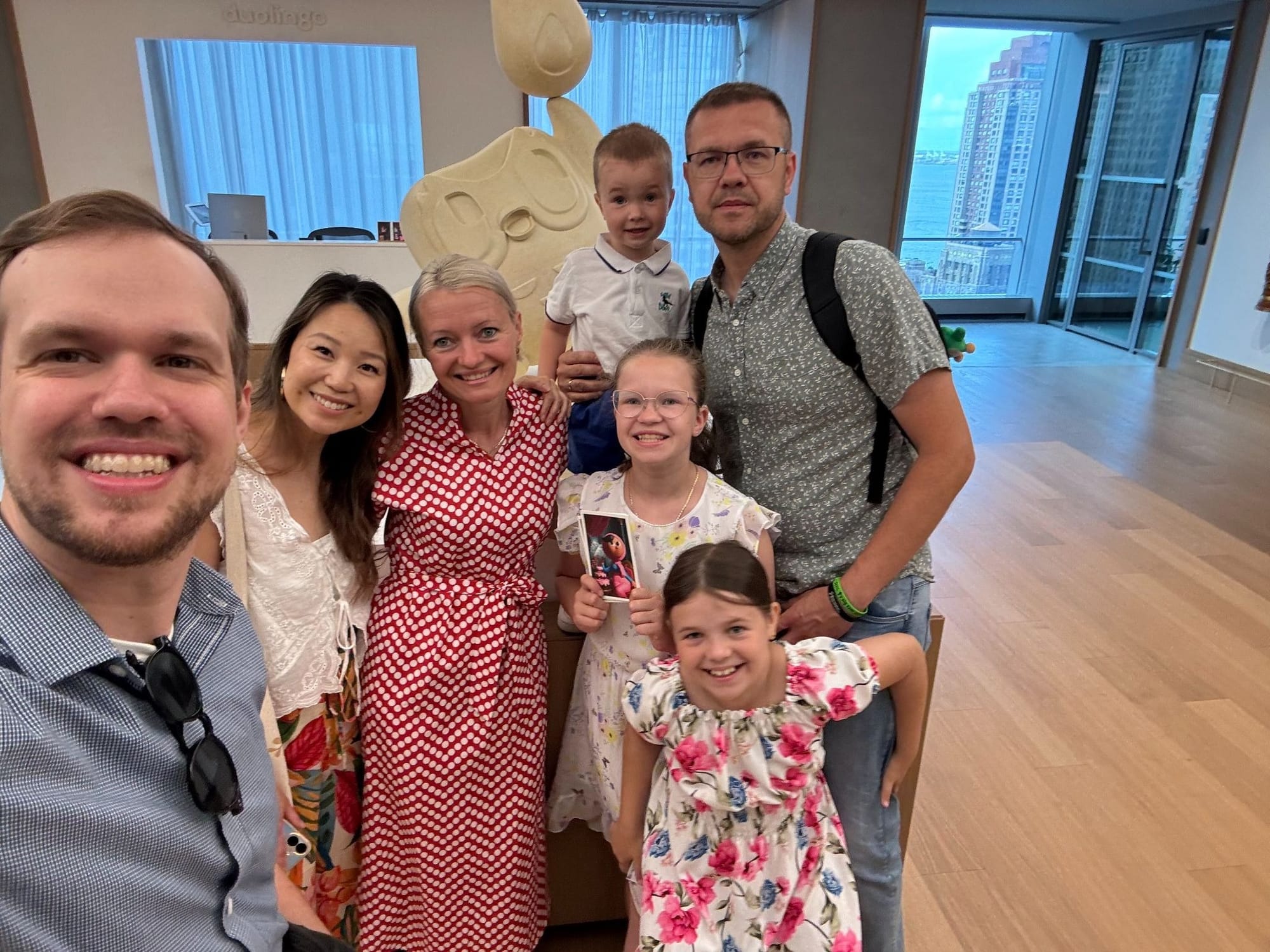 Mi novia, Brianne, y yo con Michał, su esposa Justyna y sus hijos, en los pasillos de las oficinas de Duolingo en Nueva York, con una estatua de Duo en el fondo y edificios altos detrás de la ventana.