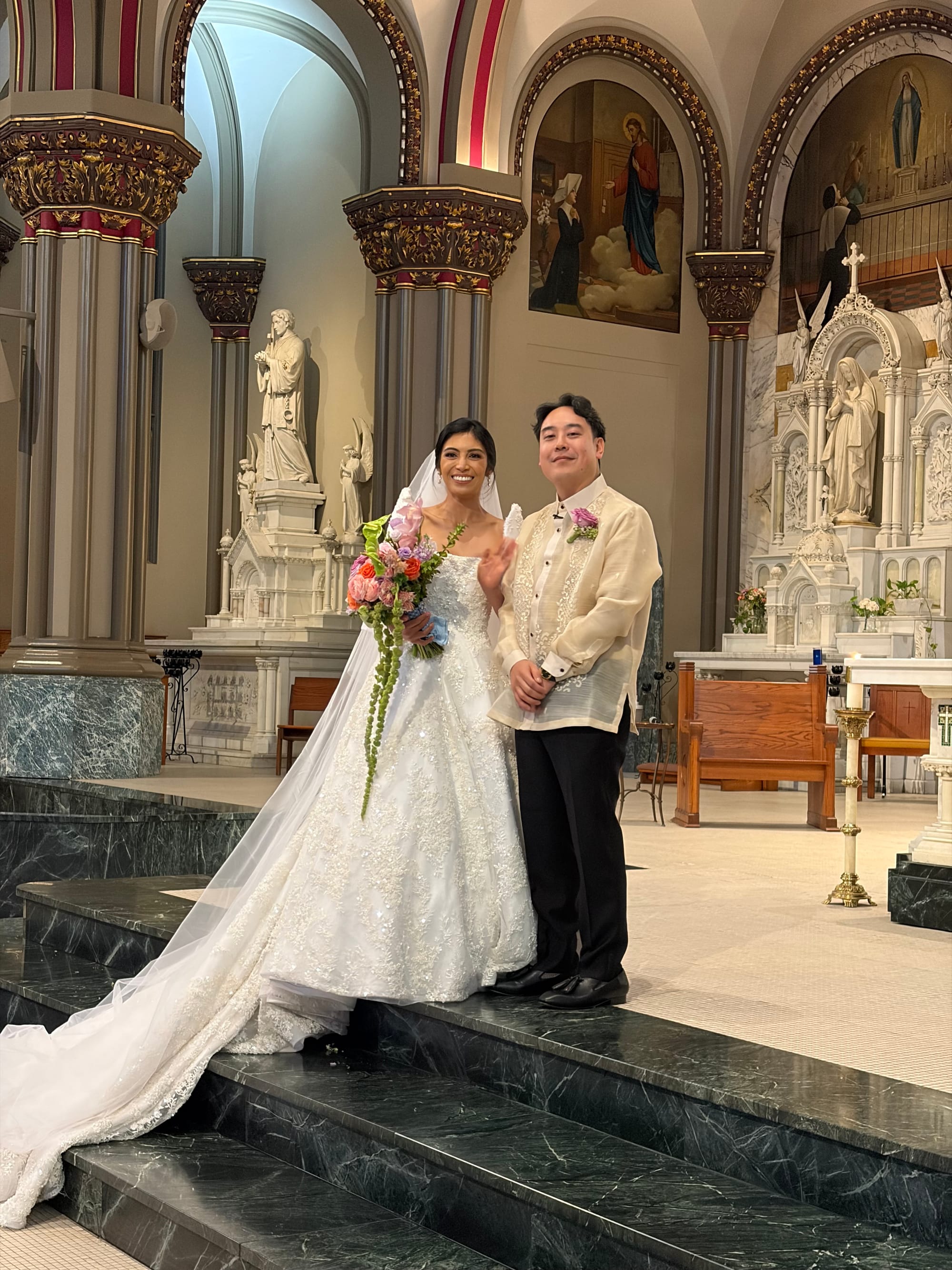 Photo of Alexa and Daryl in wedding attire. Both are smiling at the camera and Alexa is waving.