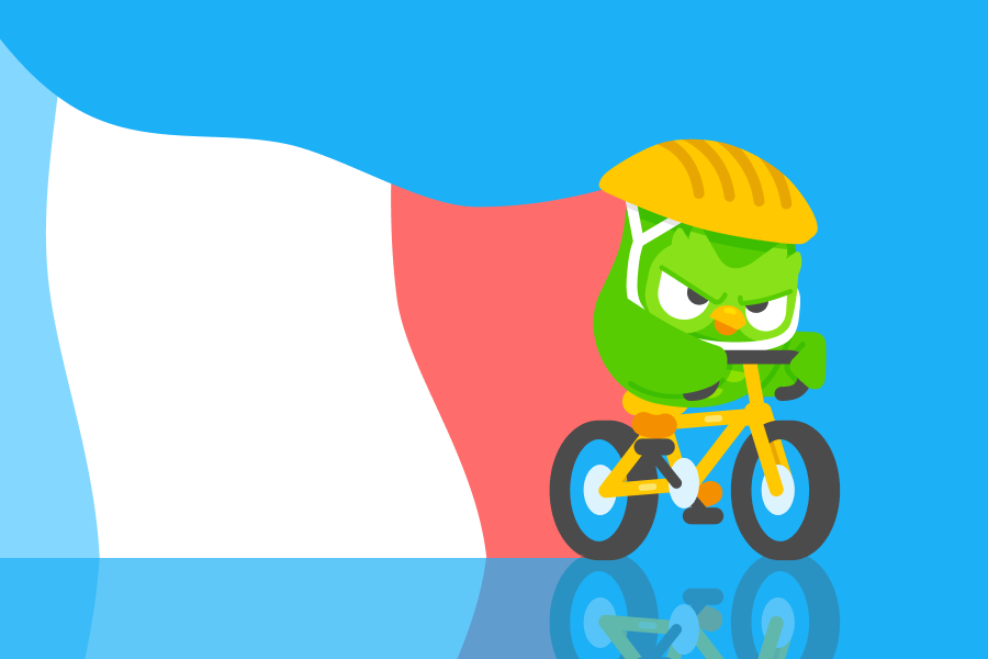 Duo the owl is wearing a yellow helmet and riding a bike with a determined look on his face. A French flag flies behind him.