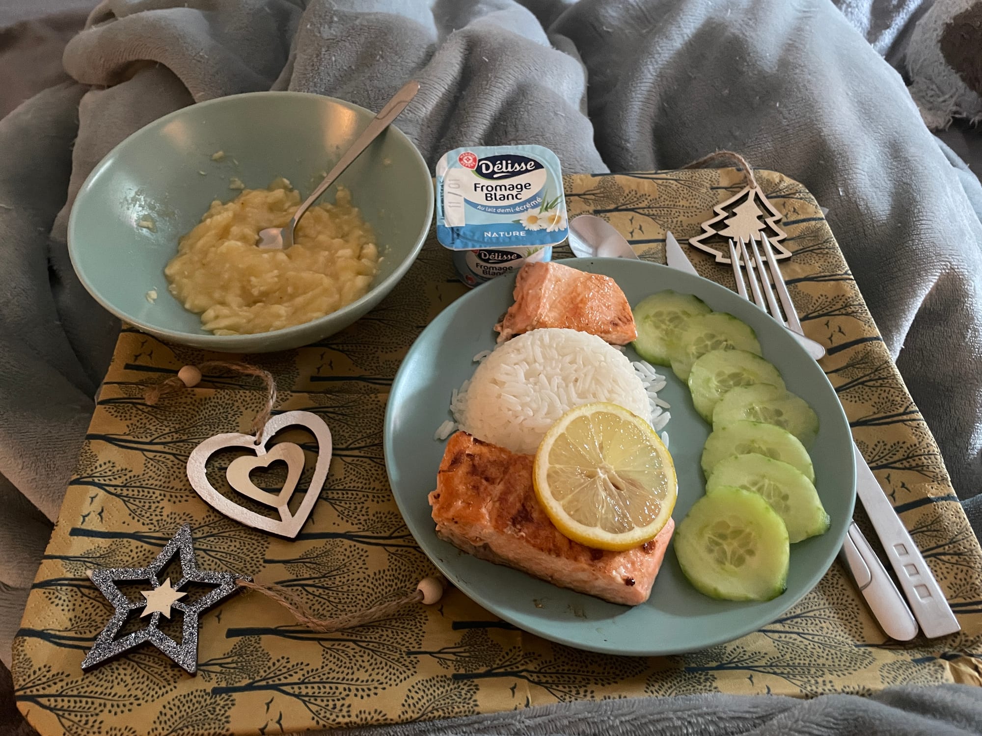 Photo d'un plateau avec une assiette (saumon, riz, concombre, compote de banane) et de petites décorations de Noël.