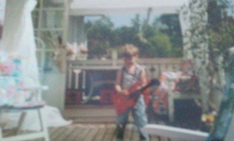 suddigt foto på mig när jag är kanske 3–5 år, på en veranda, med en leksaksgitarr i handen