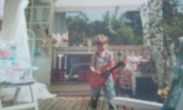 suddigt foto på mig när jag är kanske 3–5 år, på en veranda, med en leksaksgitarr i handen
