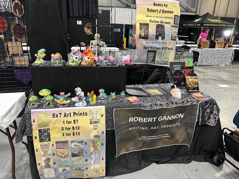 Vendor booth at NJ HorrorCon featuring 3D sculptures, a book of art prints, and a rack of books. 