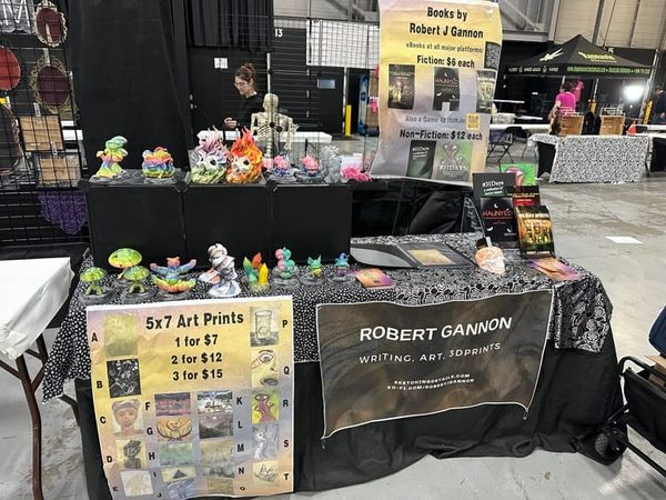 Vendor booth at NJ HorrorCon featuring 3D sculptures, a book of art prints, and a rack of books. 