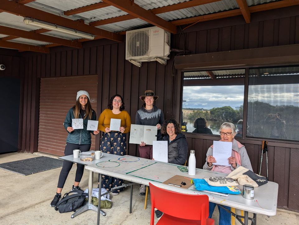 Group photo of people holding up their nature journal pages in front of building.