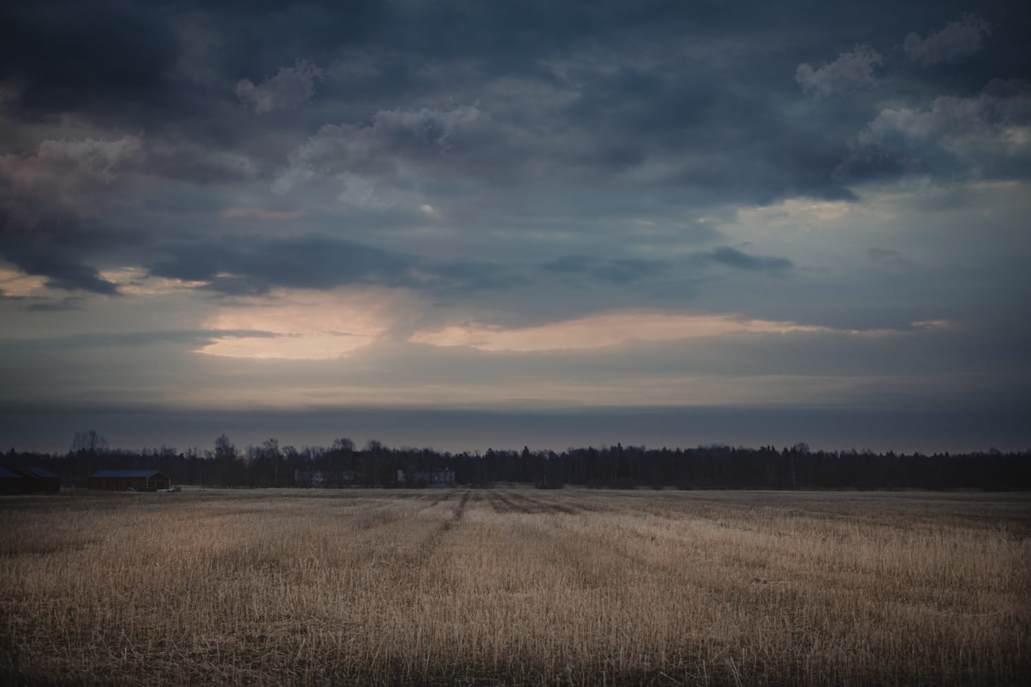 A dark open field beneath dramatic storm clouds with warm light near the horizon.
