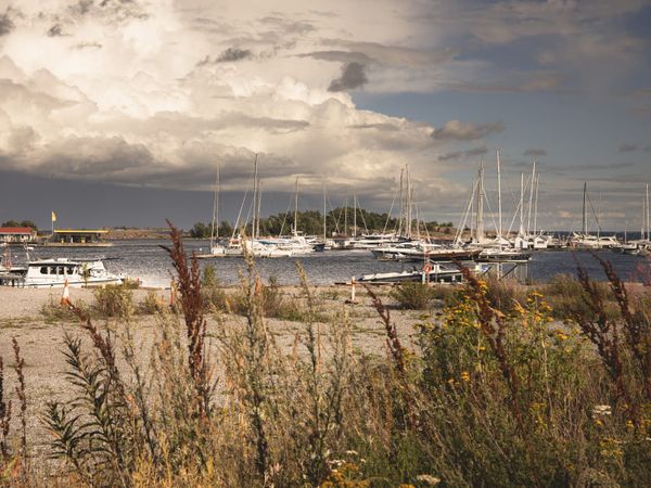 Sailboats and yacht masts in a harbour beneath expansive cloudy skies, creating a sense of journey and horizon.