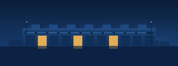 A long low shallow-bay multi-tenant industrial building at dusk with a row of roll-up dock doors