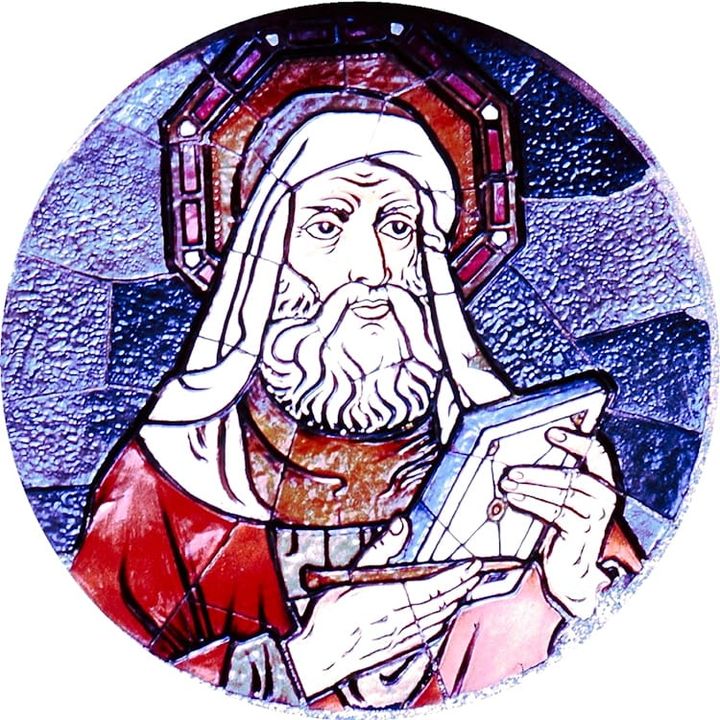 Blue artwork that looks like stained glass features a solemn bearded, haloed dignitary in a robe holding a stylus and a tablet. Image by Jusben is from https://morguefile.com/p/661623