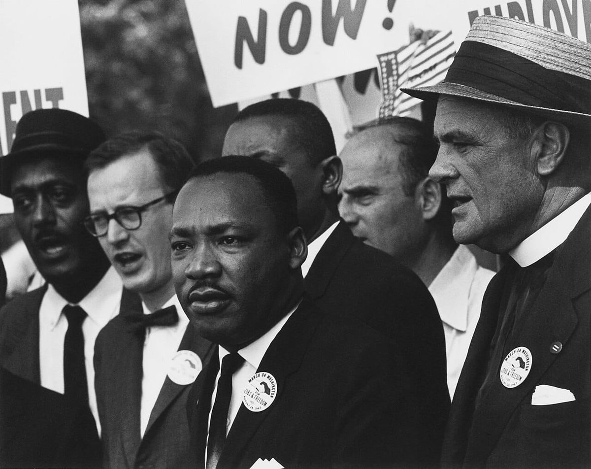 Dr Martin Luther King Jr in front of a multiracial crowd wearing suits