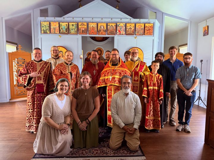 A photo of Orthodox clergy dressed in red vestments. They are surrounded by members of a choir in the nave of the St. Catherine Orthodox Mission.