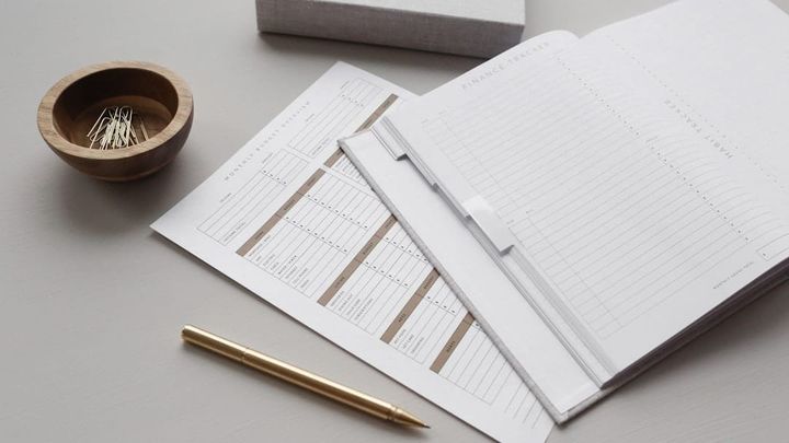 A flat-lay of printed forms and a gold pen beside a small wooden bowl of paperclips on a light desk, evoking paperwork ready to read and sign.