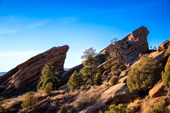 Tilted red sandstone rock formations with pines on a Colorado Front Range foothills slope under a clear blue sky.