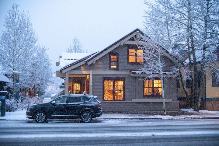 A warm-lit craftsman single-family home on a snowy Colorado street at dusk, a car parked out front