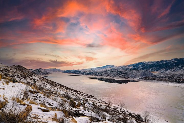 A reservoir ringed by snow-dusted foothills under a pink and purple winter sunrise, in the Larimer County Front Range near Loveland.