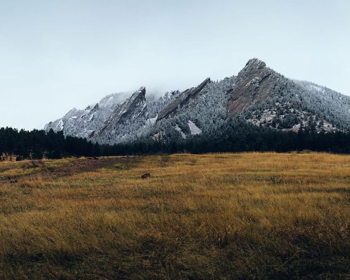 A golden open-space meadow below the snow-dusted Flatirons foothills near Boulder, Colorado