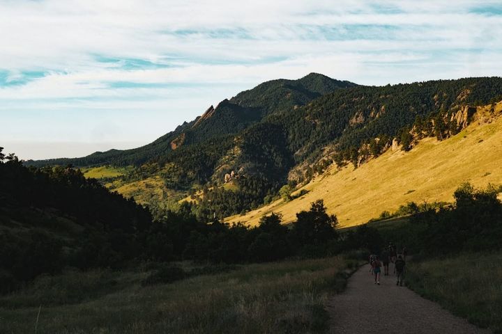 A Boulder foothills open-space trail leading toward the green mountains, with people walking in golden evening light
