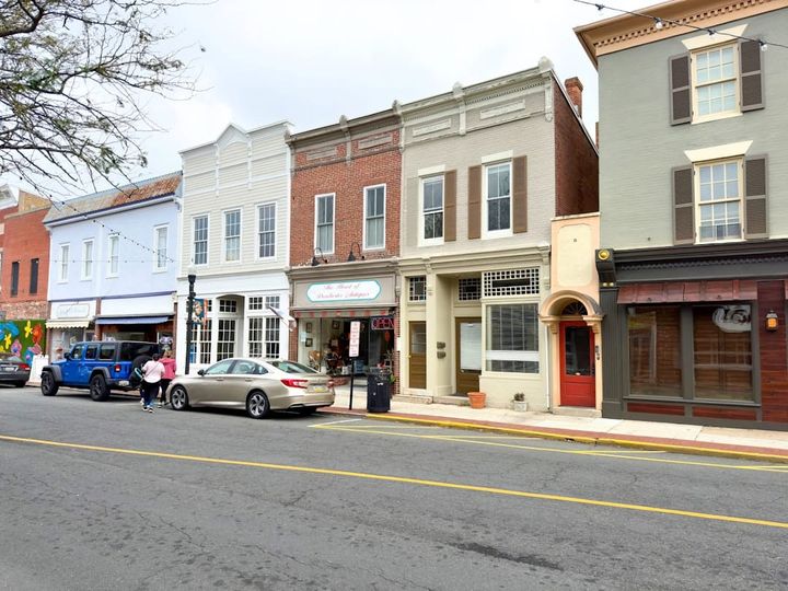 A historic small-town Main Street block of brick and painted storefronts with shops, string lights, and parked cars.