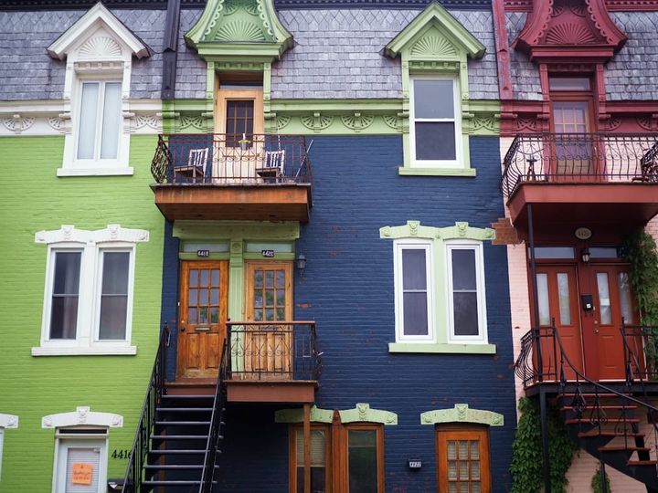 A row of brightly colored attached townhouses with ornate trim, small balconies, and exterior staircases.