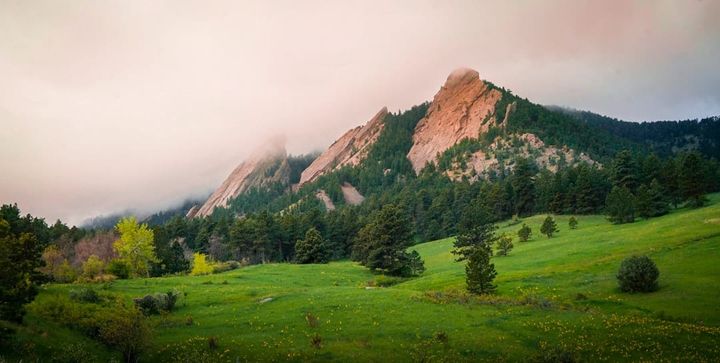 The Flatirons rising above a green foothills meadow in south Boulder, Colorado, with low cloud on the peaks