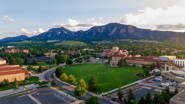 An aerial view of the University of Colorado Boulder campus with the Flatirons rising behind it