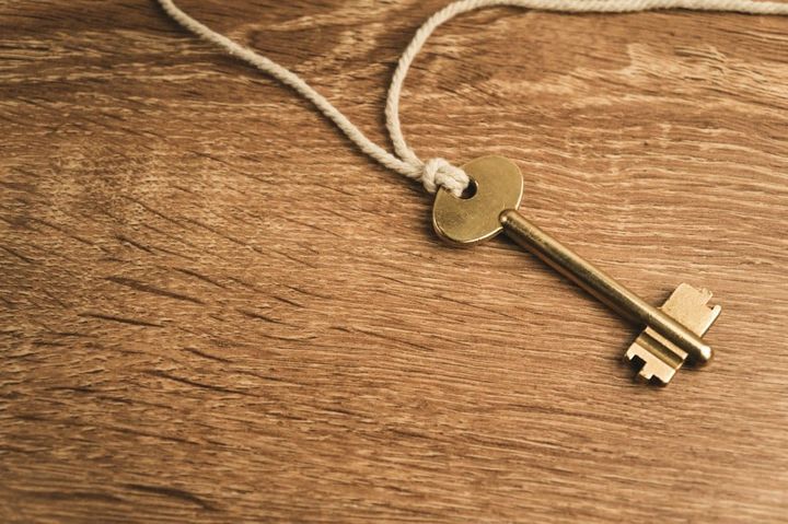 A single brass key tied to a white cord, lying on a wooden table
