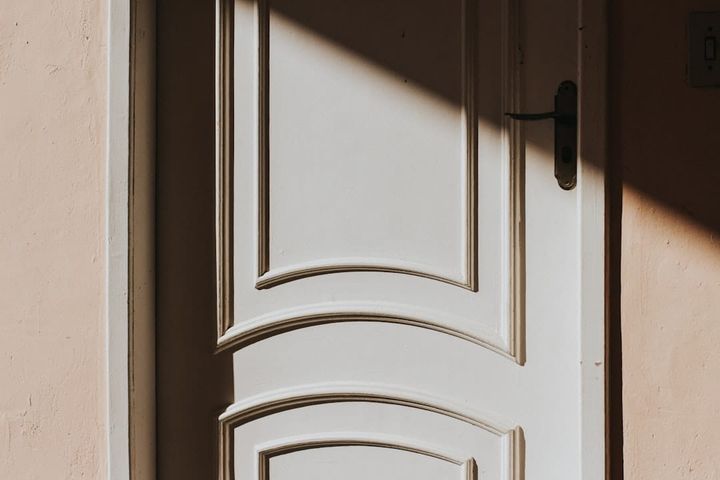 A closed white panelled door shot straight on, with a dark lever handle at its edge and warm side light falling across the panels.