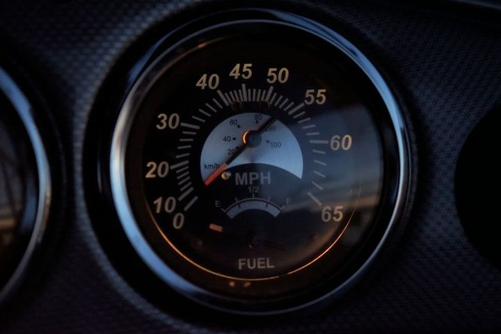 Close-up of a round car speedometer in low light, its needle near the low end of a miles-per-hour scale, with a small fuel gauge set into the lower part of the same dial.