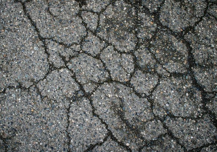 Close-up of worn gray asphalt crazed with a web of interconnected cracks