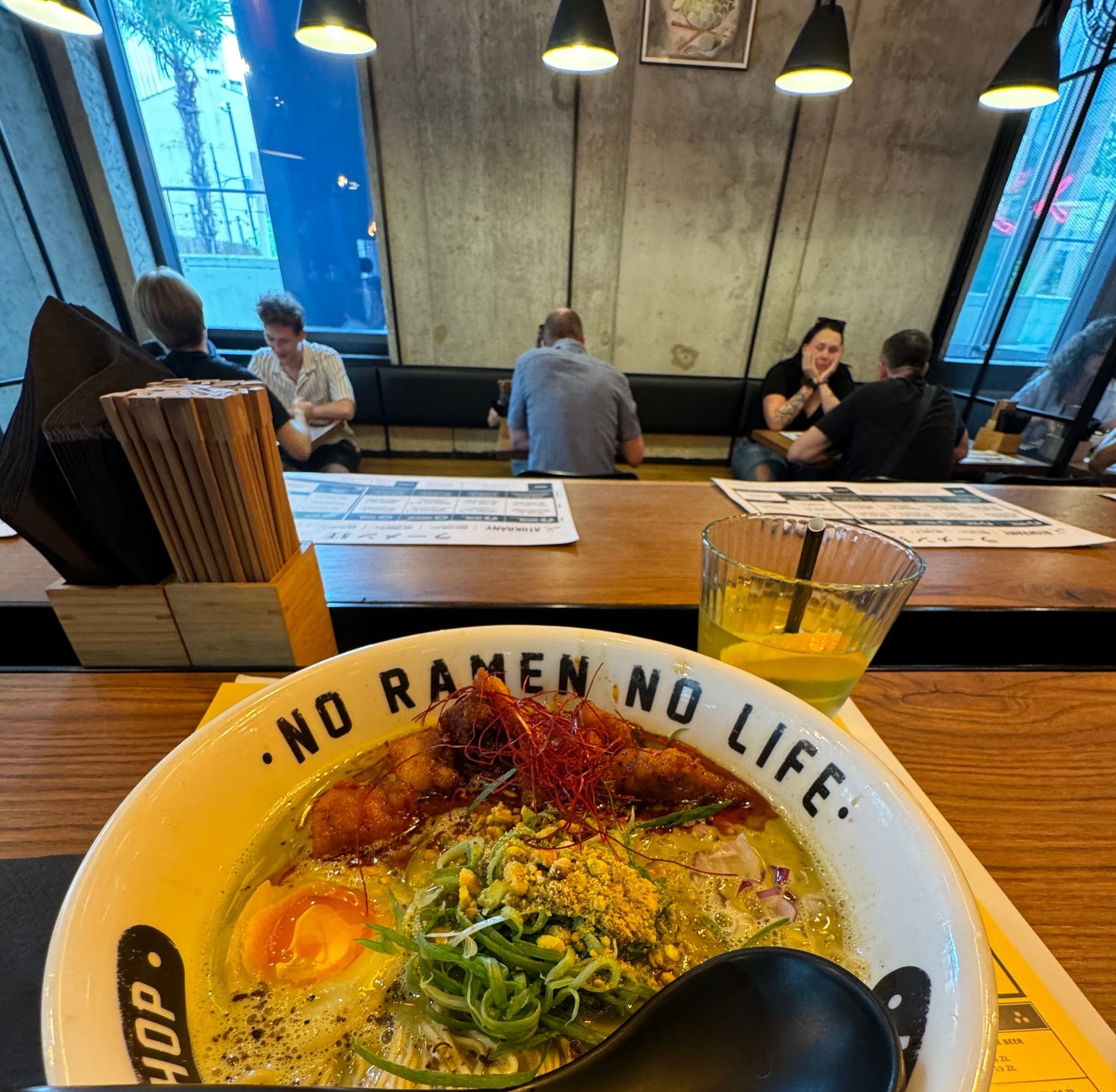 A bowl of ramen at a counter with other diners sitting together in the background.
