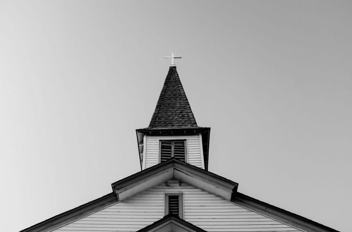 A simple church steeple looking up to the sky that balances the division of the sky.