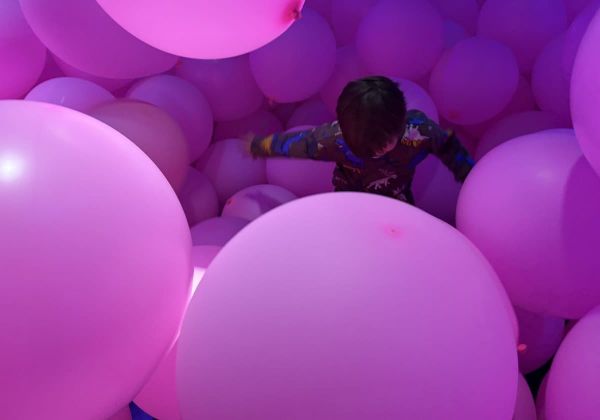 A child wading among giant pale pink balloons that fill the room.