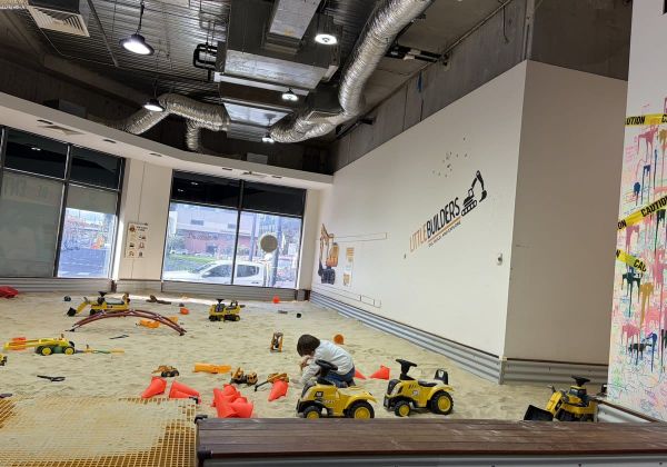 A large indoor sandpit play space, almost empty, with ride-on diggers and orange cones scattered across the sand.
