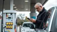 Driver checking a phone beside a petrol pump on a UK forecourt
