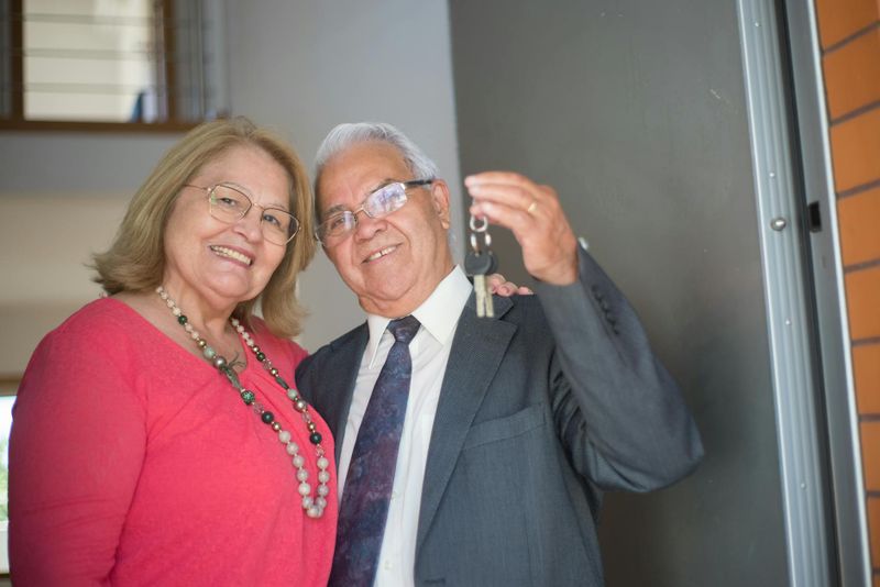 An older couple holding keys outside their home