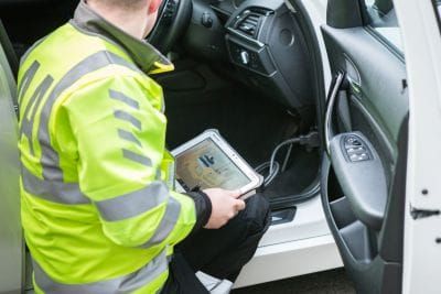 A mobile mechanic plugs a diagnostic reader into a car on a suburban driveway