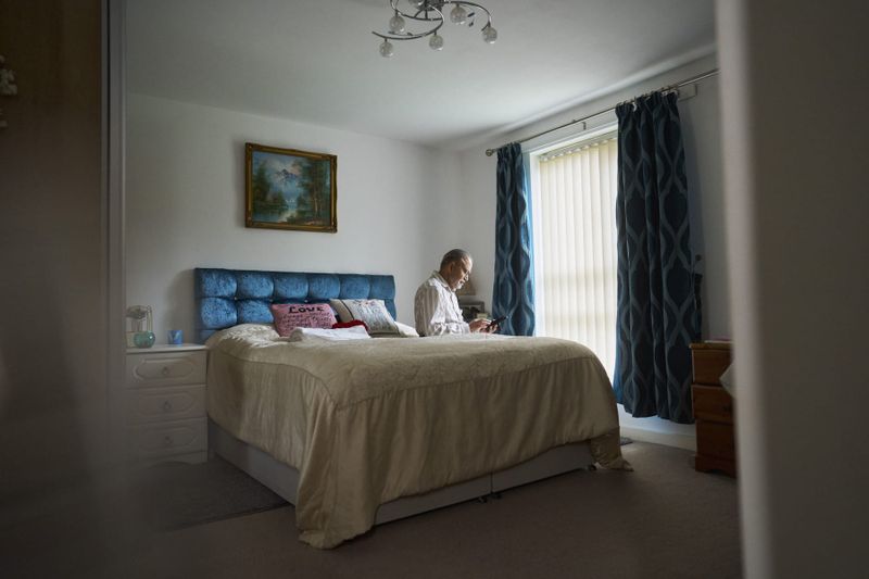An older man answers a corded telephone in a bedroom at home