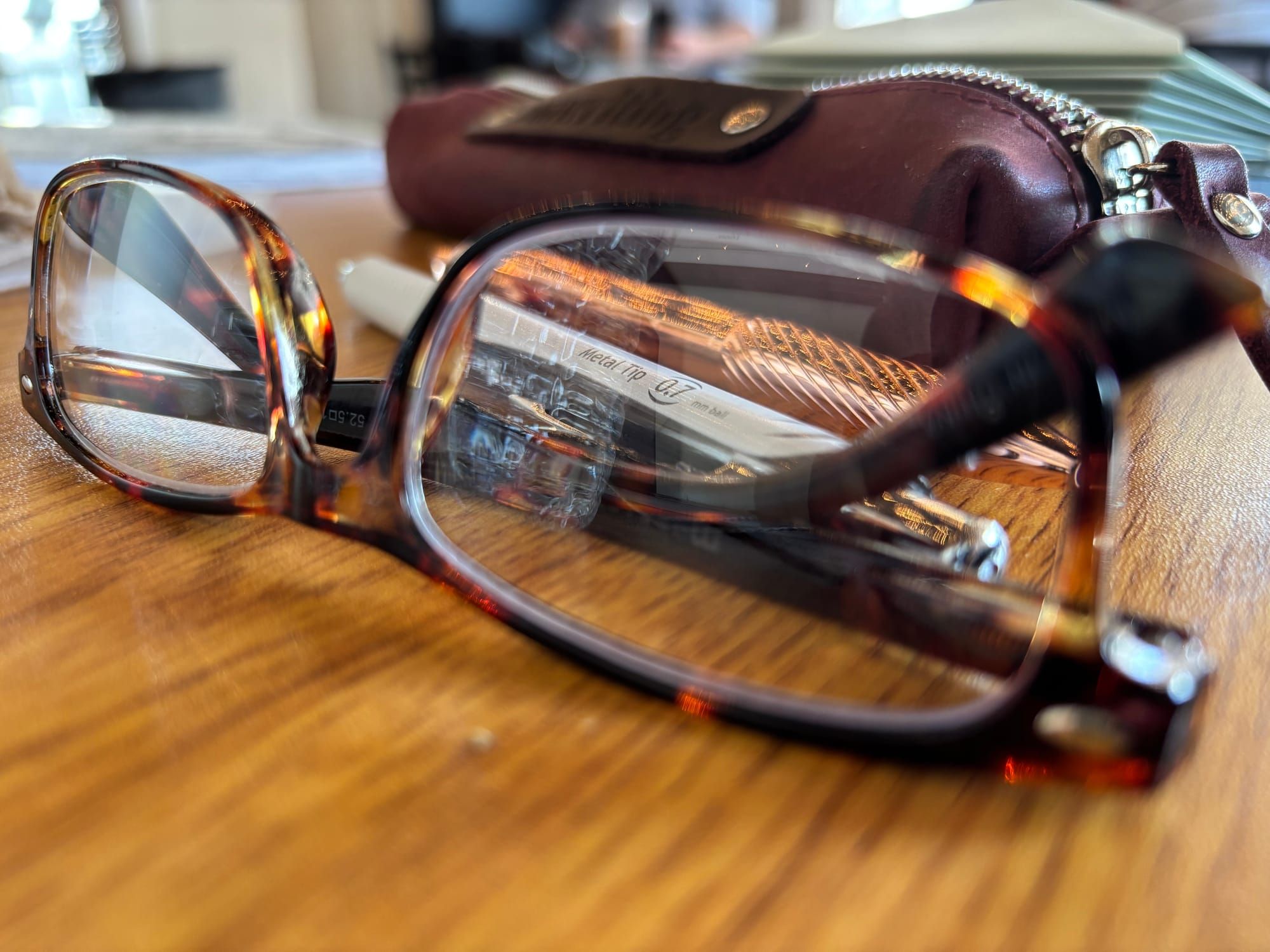 pair of glasses, pens, and a stack of letters on a table inside a café