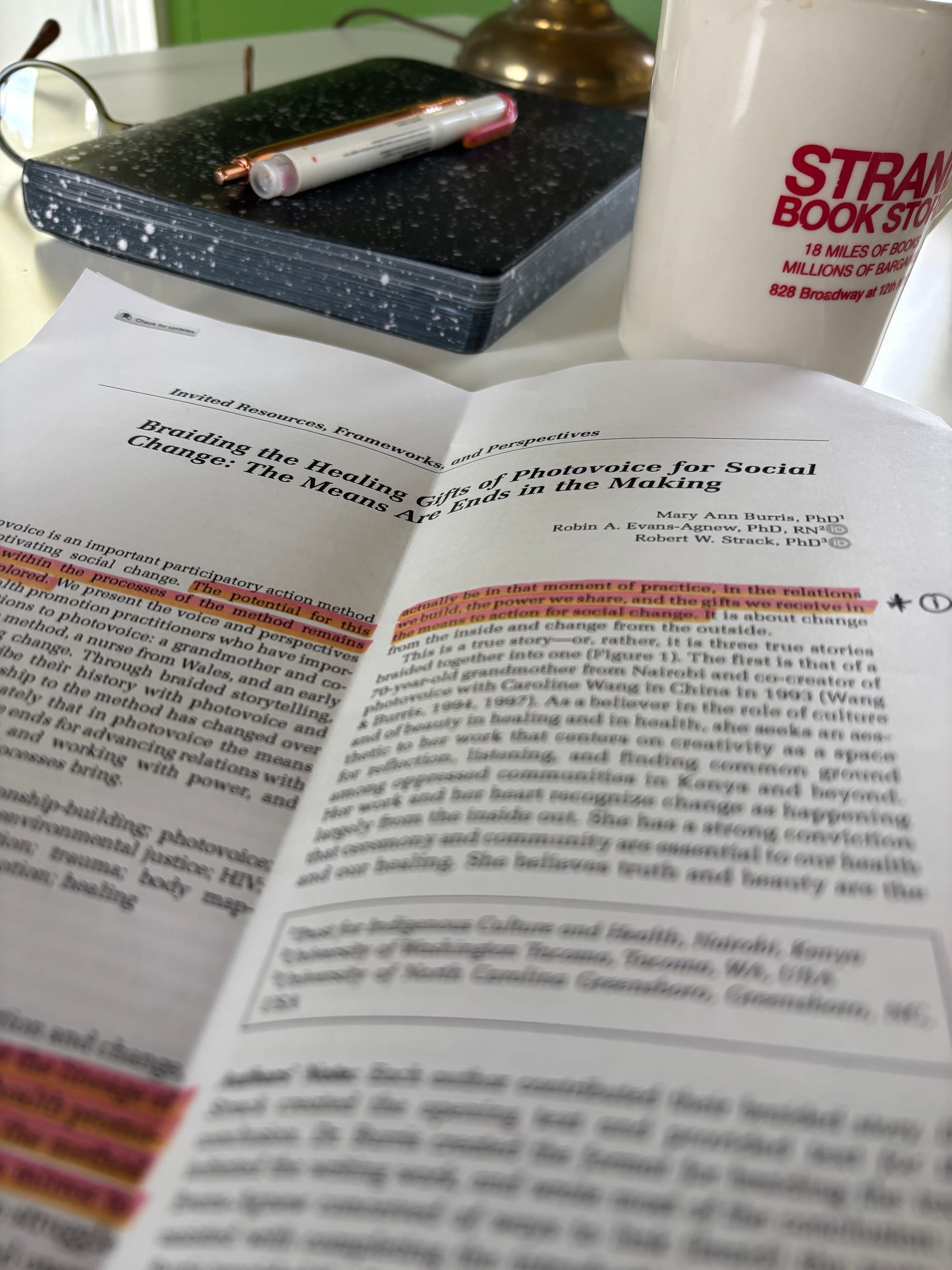 first page of a journal article with highlighted portions and marginalia atop a writing desk