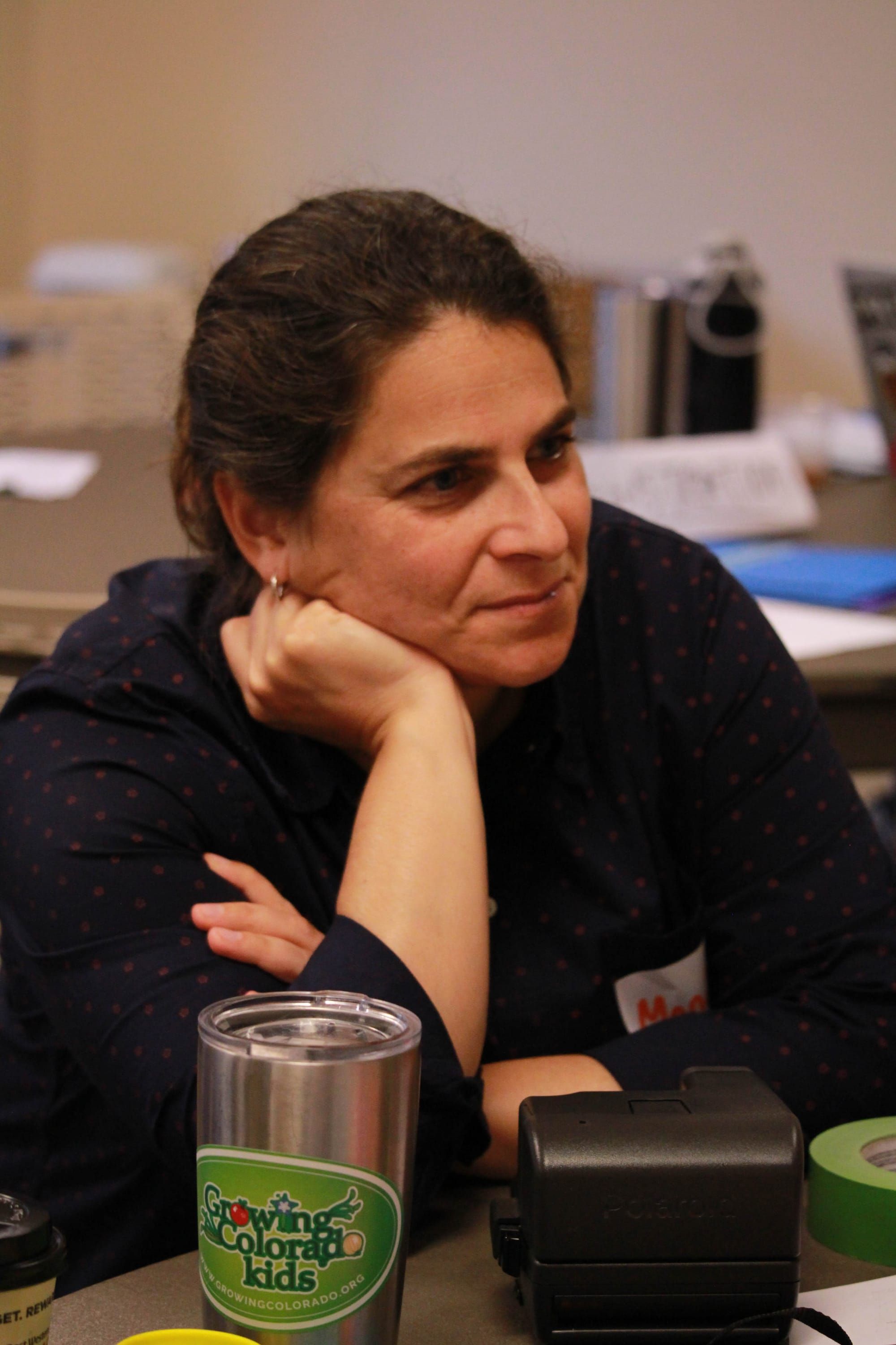 middle-aged woman with brown hair sitting at a table resting her chin on the heel of her hand