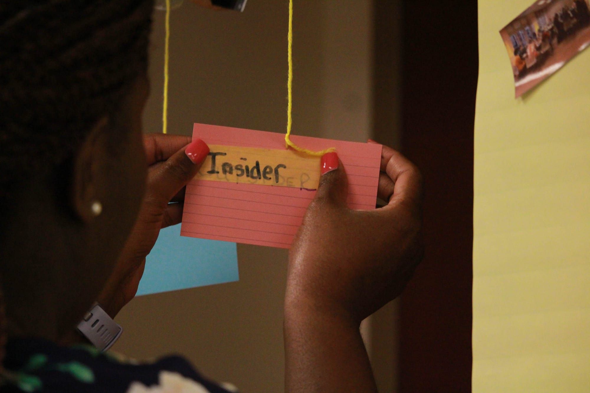 back of woman holding a pink index card with the word insider written on a piece of masking tape covering the word outside written on the index card