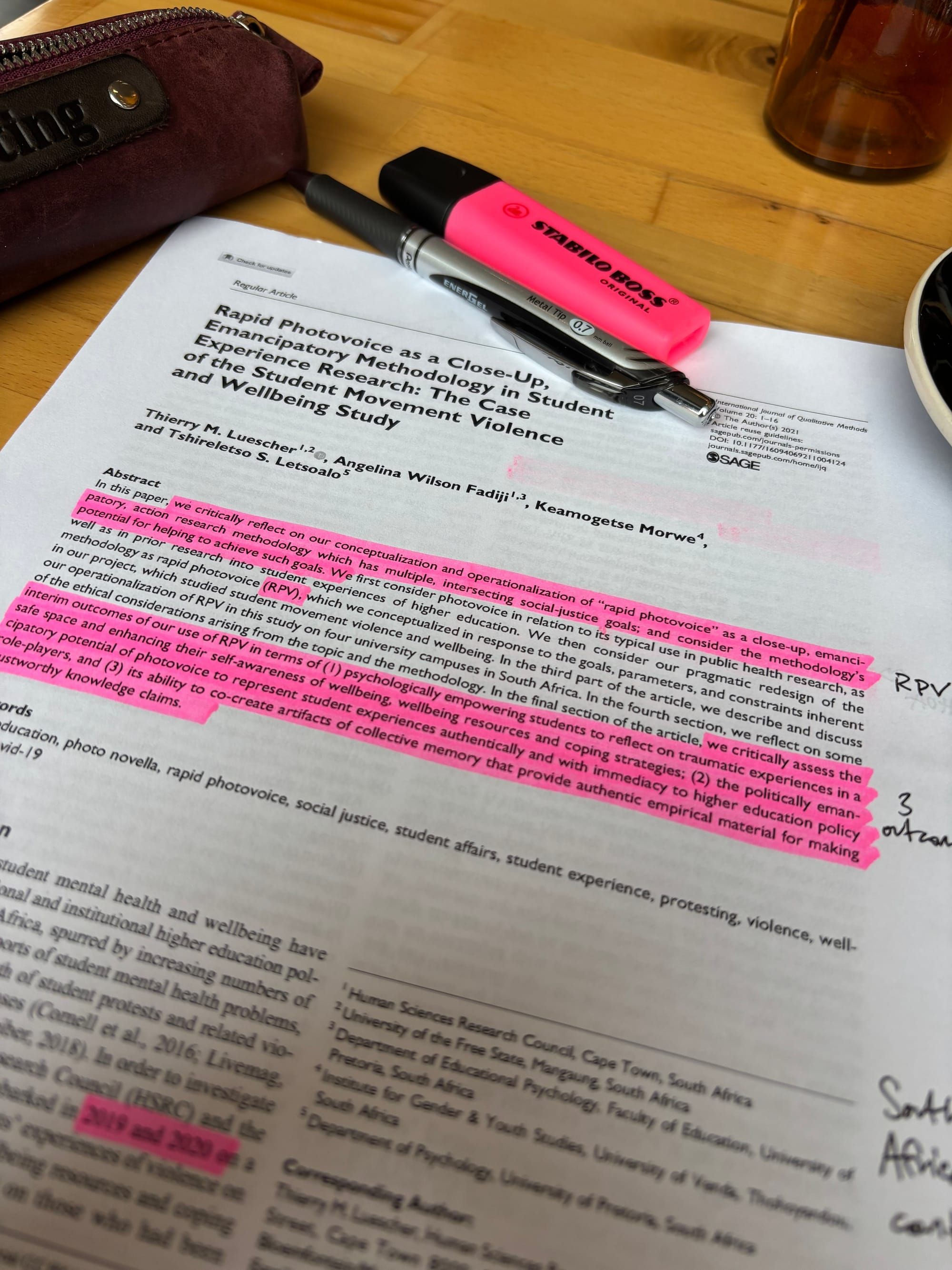 first page of the article referenced in the article with marginalia added sitting atop a wooden table with pencil case, pen, and highlighter in the background