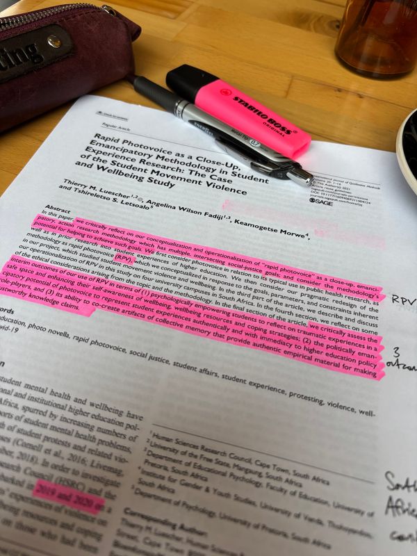 first page of the article referenced in the article with marginalia added sitting atop a wooden table with pencil case, pen, and highlighter in the background