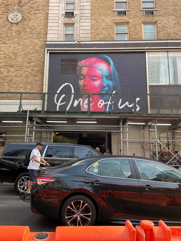 Prima Faces project artwork hung on a building in New York City; black cars and a man on a scooter are in the foreground