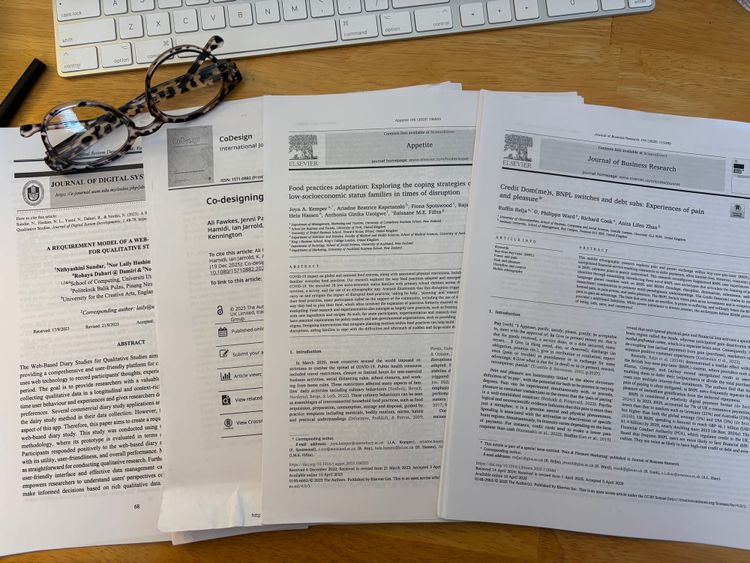 four journal articles printed out and laid onto a wooden desk