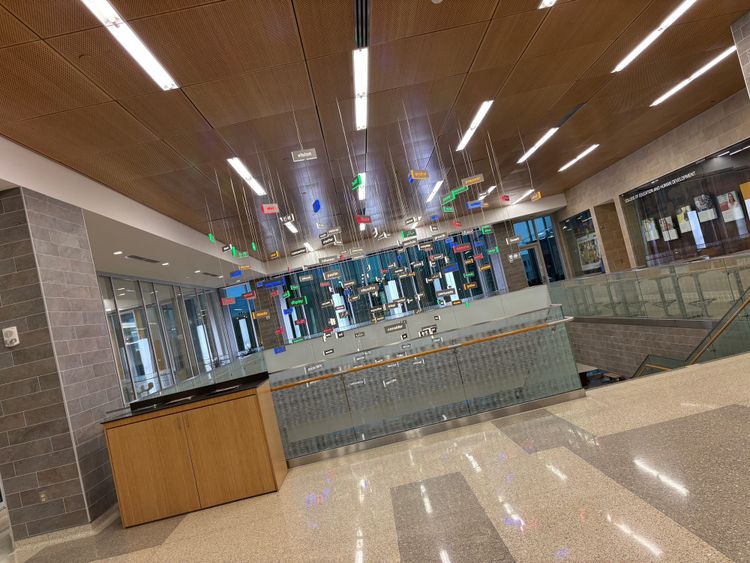 art installation inside a university building featuring illuminated and colorful words related to education hung from the ceiling