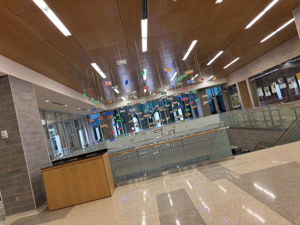 art installation inside a university building featuring illuminated and colorful words related to education hung from the ceiling