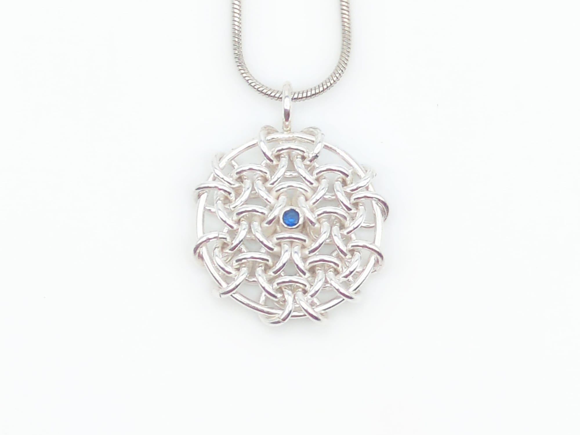 A pendant made of 7 hexagons, one in the center and 6 around it, and larger ring through the outermost edges to hold it flat. A single gemstone is set inside the central space.