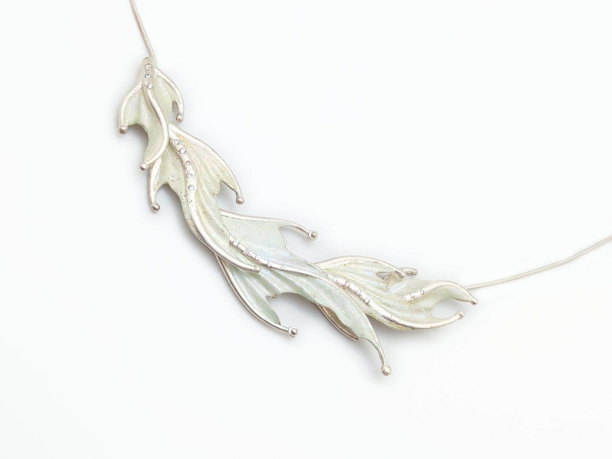 "Soap Bubble" is a fancy, flowing silver necklace. It is composed of 5 'fish fin' shapes that overlap. Each fin has a sinuous curving shape, a line of gemstones down the center, and a smooth and shiny enamel coating.