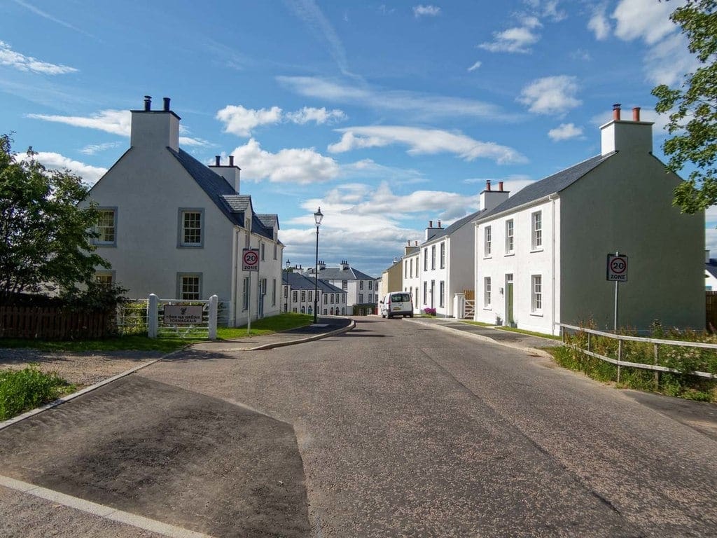 White-harled new houses along a quiet street at Tornagrain new town near Inverness under a blue summer sky